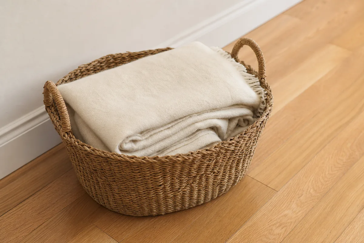 Panier en osier garni de sa couverture écrue posé sur le parquet clair